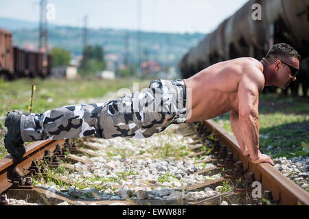 Gut aussehender Mann tun Liegestütze bei Railroad Stockfoto
