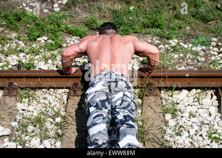Gut aussehender Mann tun Liegestütze bei Railroad Stockfoto
