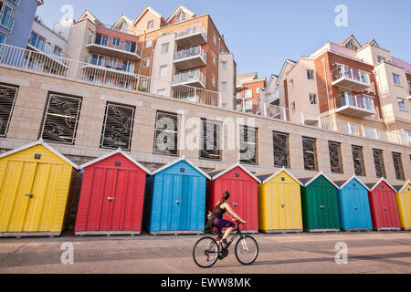 Radfahrer auf dem Fahrrad mit bunten Strandhäuschen und modernen Apartments/Wohnungen am Strand Honeycombe Entwicklung neben Boscombe Rad- Stockfoto