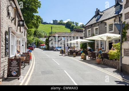 Geschäfte und eine Kneipe in Castleton mit Peveril Castle auf dem Hügel mit Blick auf das Dorf im Sommer, Derbyshire, Peak District National Park, England, Großbritannien Stockfoto