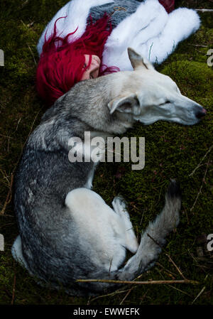 Der Stoff aus dem Träume und Alpträume: ein Junge rote kurzhaarige kaukasischen Frau Mädchen allein in einem dunklen Kiefernwald mit einem weißen Wolf-ähnlichen Hund schlafen Stockfoto