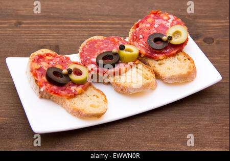 Bruschetta mit Salami und Oliven auf Holztisch Stockfoto