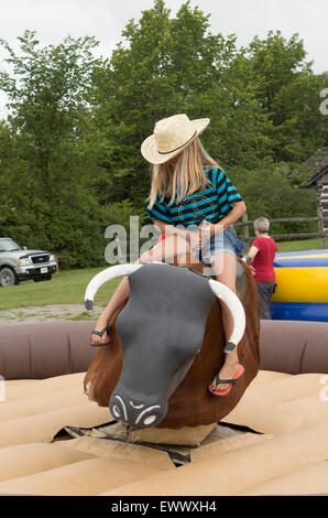 Pre-teen Mädchen reitet auf einem mechanischen Bullen bei den Canada Day Feierlichkeiten in Cannington, Ontario Stockfoto