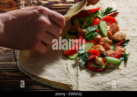 Männerhände Verpackung traditionelle Shawarma wickeln mit Huhn und Gemüse Stockfoto