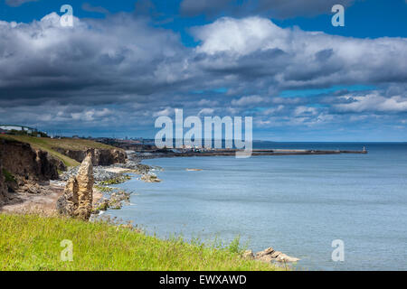 Seaham Hafen mit Klippen beleuchtet bei schwachem Licht, Sunderland in der Ferne unter einem bewölkten und blauen Himmel, County Durham, England, UK Stockfoto