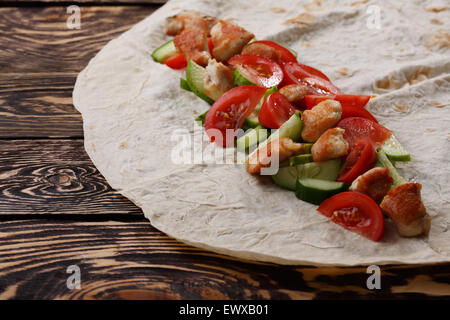Traditionelle Shawarma Wrap mit Hähnchen und Gemüse auf Holztisch kurz vor Umhüllung Stockfoto