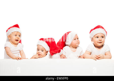 Vier Babys stehen in einer Zeile Abnutzung roten Weihnachtsmützen Stockfoto