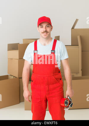 Porträt der glückliche junge Bote mit Kartons im Hintergrund stehen. vertikale Schuss Stockfoto