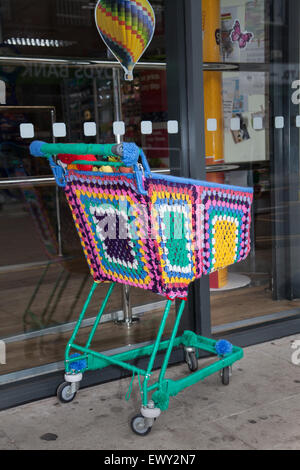 Garn - bombardiert, Yarn Bombing, yarnbombing, dekorative gestrickt, Co-op Supermarkt Einkaufswagen, Kabel Warenkorb, die Market Street. Westhoughton, Lancashire, Großbritannien Stockfoto