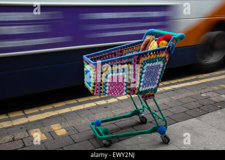 Garn - bombardiert, Yarn Bombing, yarnbombing, dekorative gestrickt, Co-op Supermarkt Einkaufswagen, Kabel Warenkorb, die Market Street. Westhoughton, Lancashire, Großbritannien Stockfoto