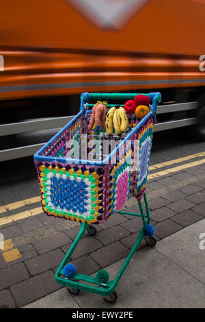 Garn - bombardiert, Yarn Bombing, yarnbombing, dekorative gestrickt, Co-op Supermarkt Einkaufswagen, Kabel Warenkorb, die Market Street. Westhoughton, Lancashire, Großbritannien Stockfoto