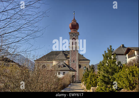 Der Luis Trenker Promenade führt bis St. Ulrich, italienisches Dorf in Dolomiten Alpen: typische Häuser, Gebäude und die roten Glockenturm mit Uhr Pfarrkirche St. Ulrich mit Bergen und grünen Koniferen im Hintergrund Stockfoto