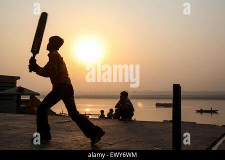 Lokalen Jungs über die Badegewässer Ghat, spielen beliebter Nationalsport Cricket bei Sonnenaufgang. Einen guten Hit und der Ball geht in den Fluss Ganges. Die Kultur von Varanasi ist eng mit dem Fluss Ganges und religiöse Bedeutung des Flusses. Es ist "die religiöse Hauptstadt des India'and ein wichtiges Wallfahrtsziel. Varanasi, auch bekannt als Benares, eine alte Stadt, eine der ältesten kontinuierlich bewohnten Städte der Welt, liegt am Ufer des heiligen Flusses Ganges links/West. Gelten als heilig durch Hindus, Buddhisten und Jains. Staat Uttar Pradesh, Indien, Asien. Stockfoto