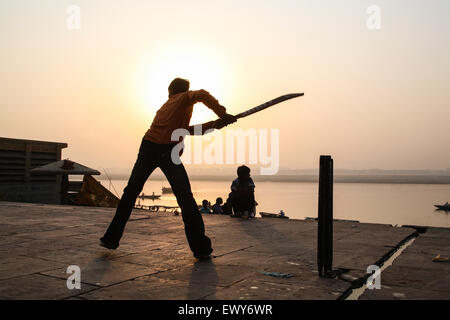 Lokalen Jungen, auf dem baden Ghat, spielen populäre nationale, Sport, der, Kricket, bei Sonnenaufgang. Eine gute schlagen und die Kugel geht in den Fluss Ganges, Varanasi, Stockfoto