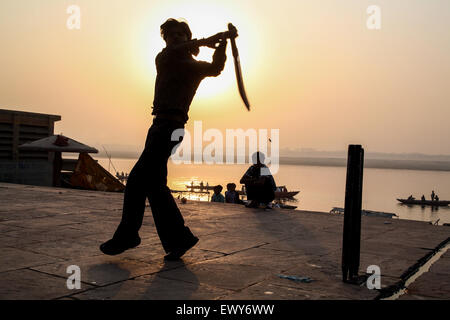 Lokalen Jungen, auf dem baden Ghat, spielen populäre nationale, Sport, der, Kricket, bei Sonnenaufgang. Eine gute schlagen und die Kugel geht in den Fluss Ganges, Varanasi, Stockfoto