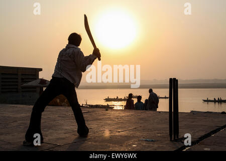 Lokalen Jungen, auf dem baden Ghat, spielen populäre nationale, Sport, der, Kricket, bei Sonnenaufgang. Eine gute schlagen und die Kugel geht in den Fluss Ganges, Varanasi, Stockfoto