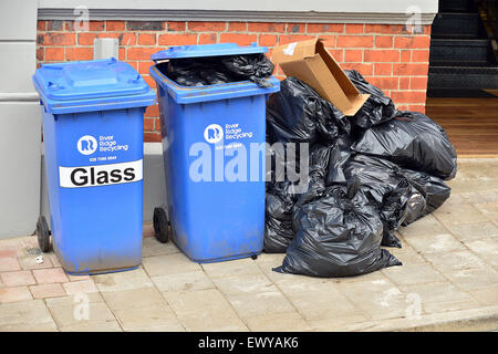 Blaue Wheelie-Kästen und schwarzen Plastiktüten mit Müll vor einem Café. Stockfoto