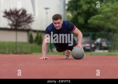 Junger Mann im Freien durchführen von Push-Ups auf Medizinball Bodybuilding Übung Stockfoto