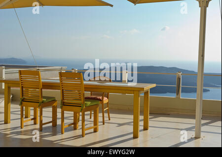 Ein Tisch und Stühle auf dem Balkon eines Restaurants mit Blick auf eine wunderschöne Landschaft auf Sonne eingestellt, Fira, Santorini, Griechenland. Stockfoto