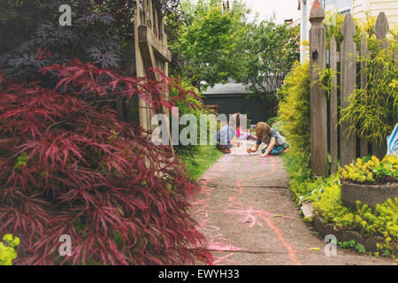 Drei kleine Kinder, die Zeichnung mit Kreide auf einem Pfad in einem Garten Stockfoto