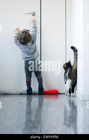 Babymädchen versucht, öffnen Sie die Tür für ihre Katze Stockfoto