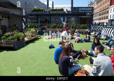 Menschen sitzen und entspannen im Sommer bei der Boxpark in Shoreditch, London, England Stockfoto