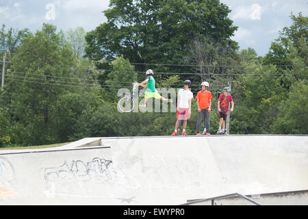 Vier Jungs im Teenageralter auf einem Skateboard-Park. Man macht einen Stunt mit seinem bmx-Rad. Stockfoto
