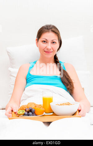 eine Frau mit einem Tablett mit Frühstück im Bett am Morgen Stockfoto