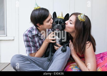 Junges Paar Hund auf Wange küssen und tragen party Hüte Stockfoto