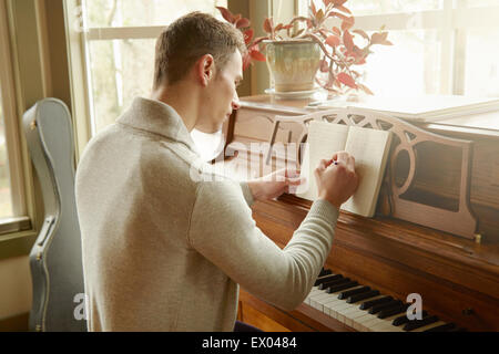 Junger Mann schreiben in Notebook während am Klavier Stockfoto
