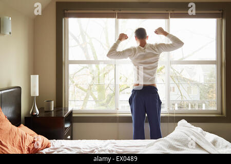 Rückansicht des jungen Mannes vor Schlafzimmerfenster Stockfoto