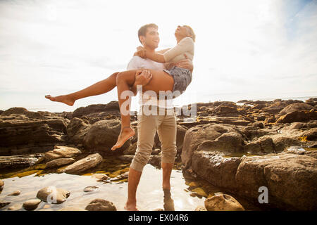 Junger Mann mit Freundin über Felsen-Pool am Strand Stockfoto