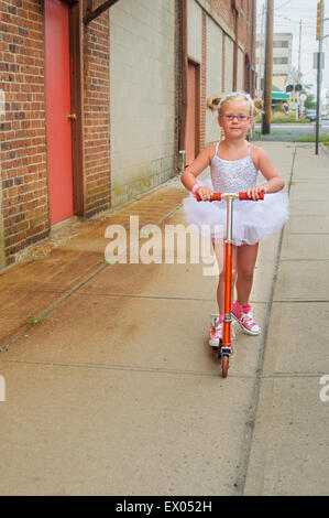 Junges Mädchen mit Tutu und rosa Baseball-Stiefeln, mit Roller Stockfoto