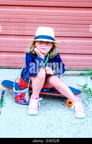 Porträt des jungen Mädchens tragen Tutu, Jeansjacke und Hut, sitzt auf skateboard Stockfoto