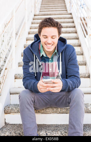 Junger Mann sitzt auf Schritte mit smartphone Stockfoto