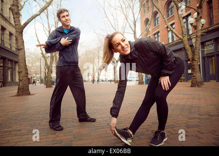 Männliche und weibliche Läufer Aufwärmen auf Baum gesäumten Straße, Pioneer Square, Seattle, USA Stockfoto