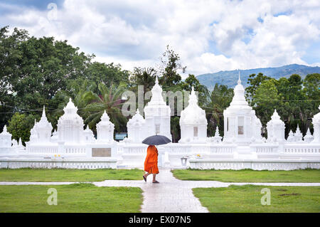 Ein Regenschirm-tragenden Mönch geht vorbei an den charakteristischen weißen Chedis des Wat Suan Dok, Chiang Mai, Thailand Stockfoto