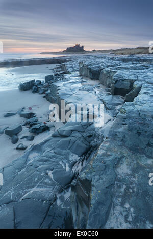 Bamburgh Castle von der felsigen Küste beschossen Bamburgh Strand bei Sonnenaufgang, Bamburgh, Northumberland, Großbritannien Stockfoto