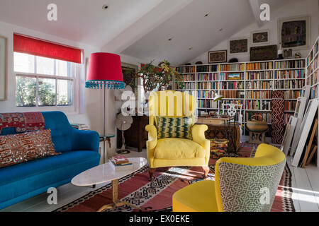 Gelbe geflügelten hinteren Sessel, Julep Stuhl und kühnen blauen Sofa im Wohnzimmer Raum mit usbekischen Kelim, Aborigine-Kunst und eingebaute Buch Sie Stockfoto