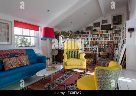Gelbe geflügelten hinteren Sessel, Julep Stuhl und kühnen blauen Sofa im Wohnzimmer Raum mit usbekischen Kelim, Aborigine-Kunst und eingebaute Buch Sie Stockfoto