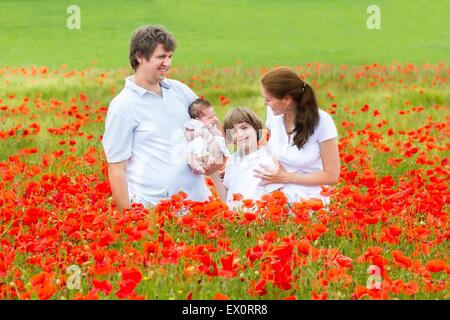 Junge schöne Familie mit einem neugeborenen Tochter und einen kleinen Sohn zu Fuß in eine rote Blumenfeld Stockfoto