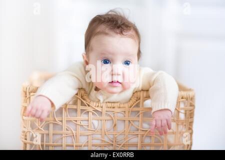 Entzückende Babymädchen mit schönen blauen Augen spielen in einen Wäschekorb Stockfoto