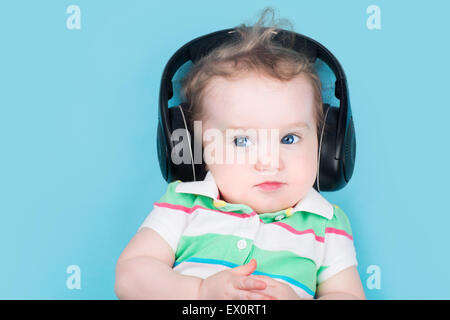 Lustige kleine Baby auf einem blauen Hintergrund tragen riesige schwarze Kopfhörer Stockfoto