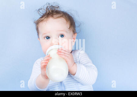 Süßes kleines Baby mit schönen blauen Augen Trinkmilch in einer Plastikflasche entspannend auf einer blauen gestrickte Decke Stockfoto