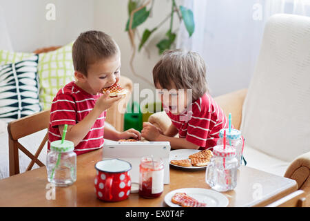 Zwei glückliche Kinder, zwei Brüder, gesundes Frühstück am Holztisch in sonnige Küche sitzen essen Waffeln und beobachtete Auto Stockfoto