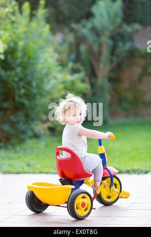 Niedliche glücklich lächelnden Baby Mädchen ihr erstes Fahrrad im Hinterhof ihres Hauses Stockfoto