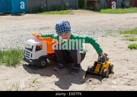 der kleine Junge in einem Bandana spielt mit Maschinen auf der Straße Stockfoto