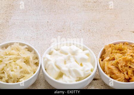 Sauerkraut, Kimchi und Joghurt - fermentiert beliebte probiotische Lebensmittel - drei Keramikschale gegen rustikales Holz mit einem Textfreiraum Stockfoto