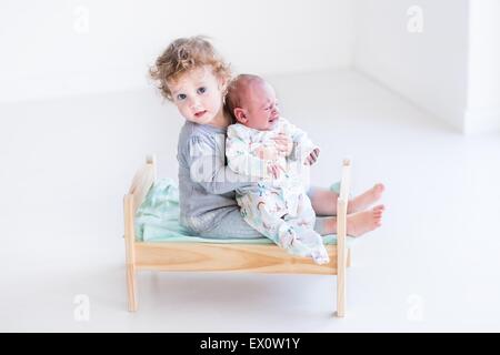 Niedlichen Kleinkind Mädchen spielen mit ihrem Neugeborenen Baby Bruder in einem Holzspielzeug Krippe Stockfoto