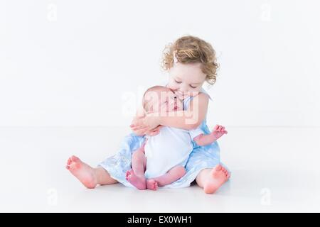 Süßes Kleinkind Mädchen in einem blauen Kleid ihr neugeborenes Baby Bruder küssen Stockfoto